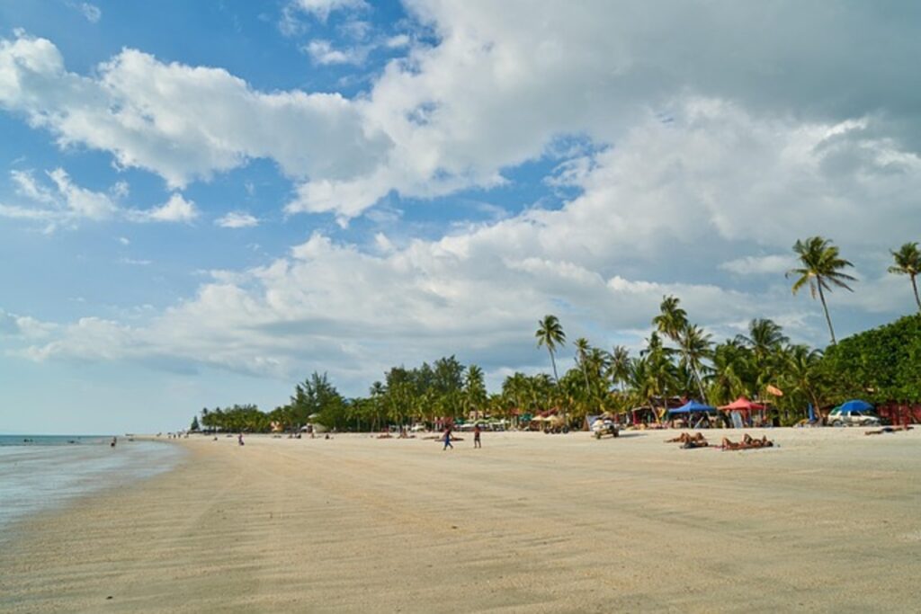 Langkawi beach with palm trees under a cloudy sky; exploring Langkawi history.