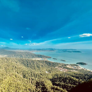 Langkawi coastline view from above, lush green hills meet the turquoise sea under a bright blue sky.