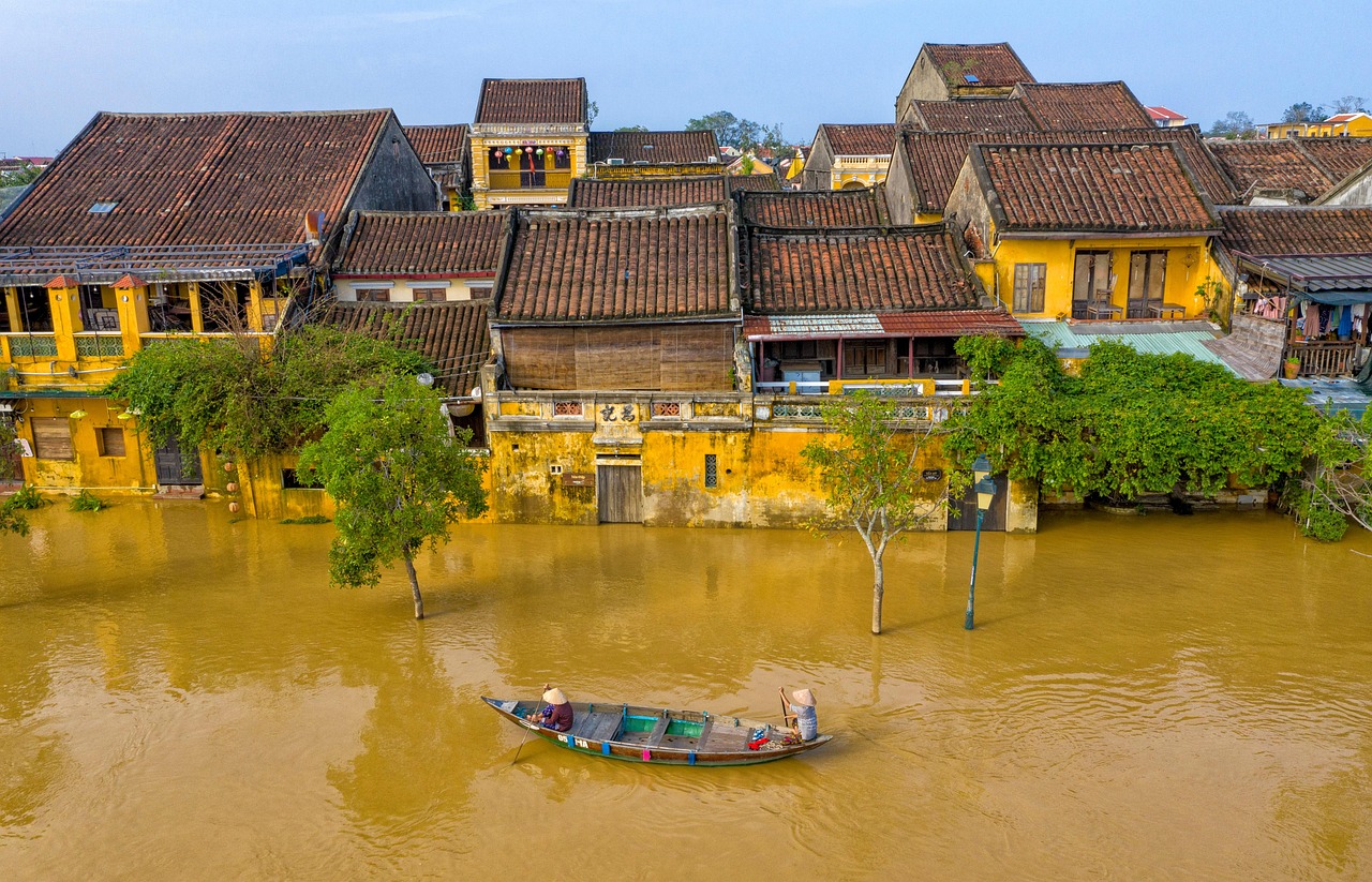 Hoi An, Vietnam, during a flood with a small boat navigating the water near historic yellow buildings.