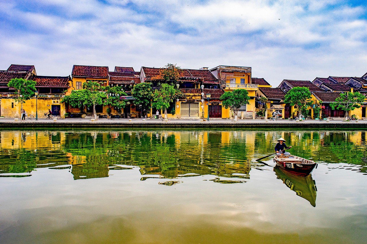 Hoi An riverside view with traditional yellow buildings reflected in the water and a boat.