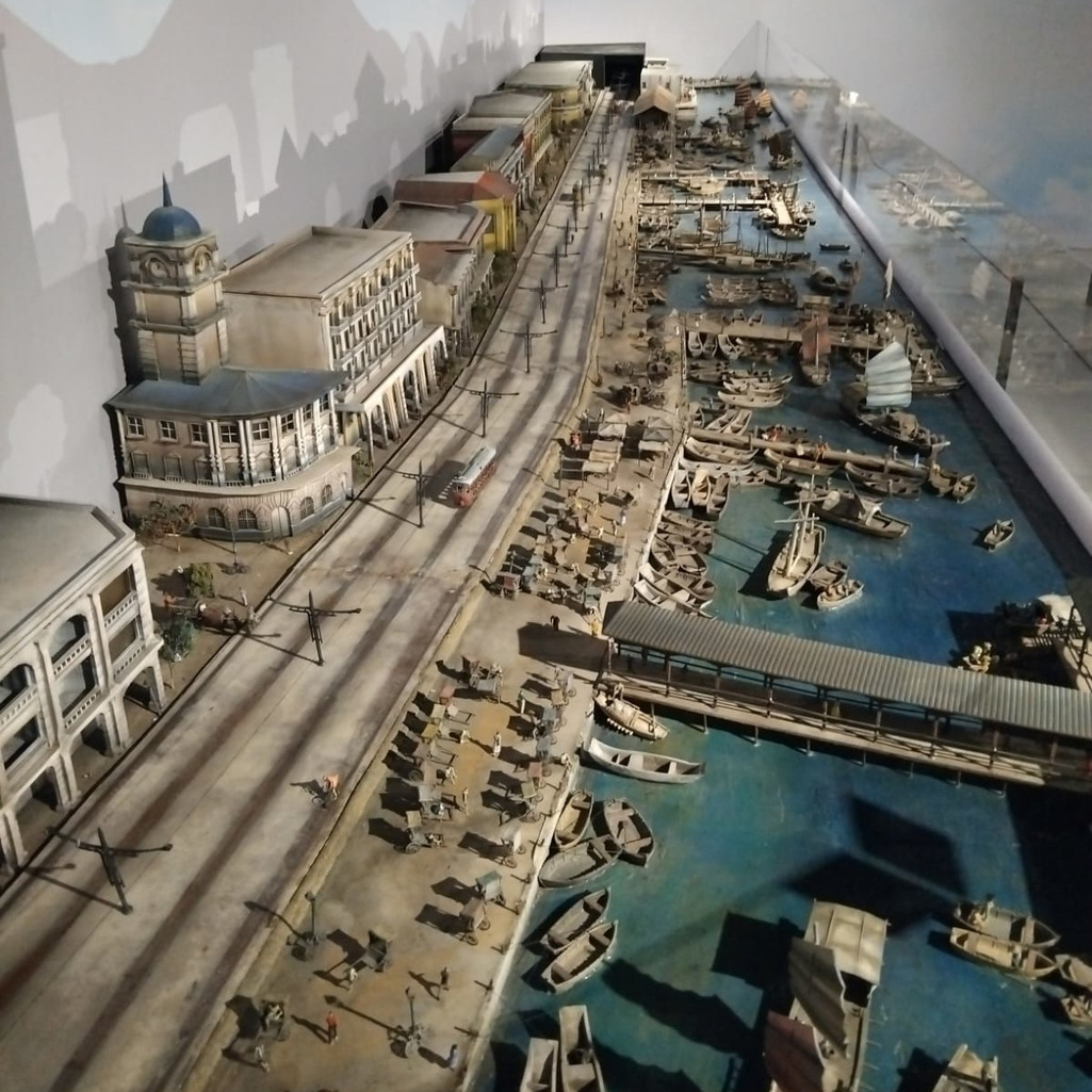 Miniature model of a historic Hong Kong harbor scene with boats and buildings.