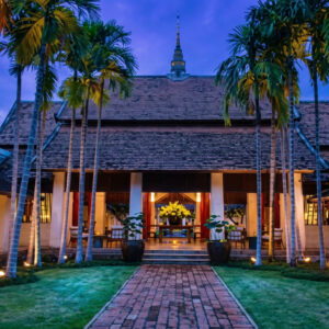 Ratchamankha Hotel entrance: Traditional Thai building with palm trees and brick pathway at dusk.