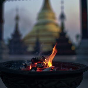 Burning coals in a censer with a blurred Buddhist temple in the background.