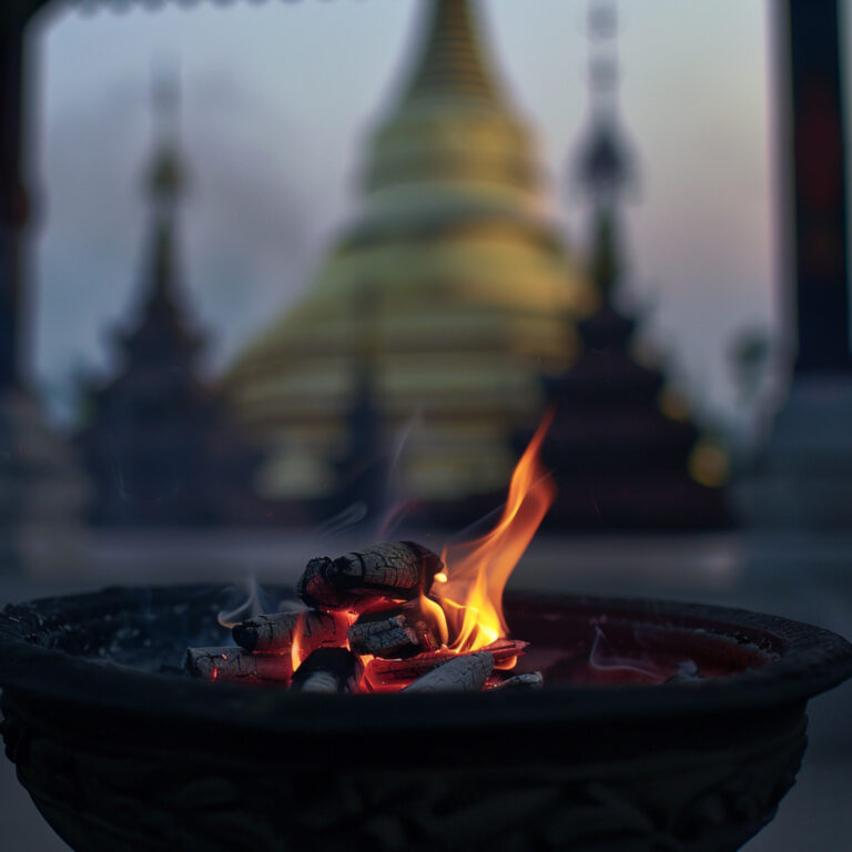 Burning coals in a censer with a blurred Buddhist temple in the background.