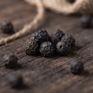 Black peppercorns scattered on a rustic wooden surface, hinting at historical spice trade and flavour migration.